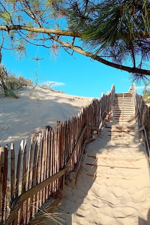 A wooden boardwalk leading through a sandy area with sparse vegetation and a clear blue sky.