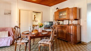 A dining area with a wooden table, chairs, and a cabinet. There is a television on the wall and a door leading to another room.