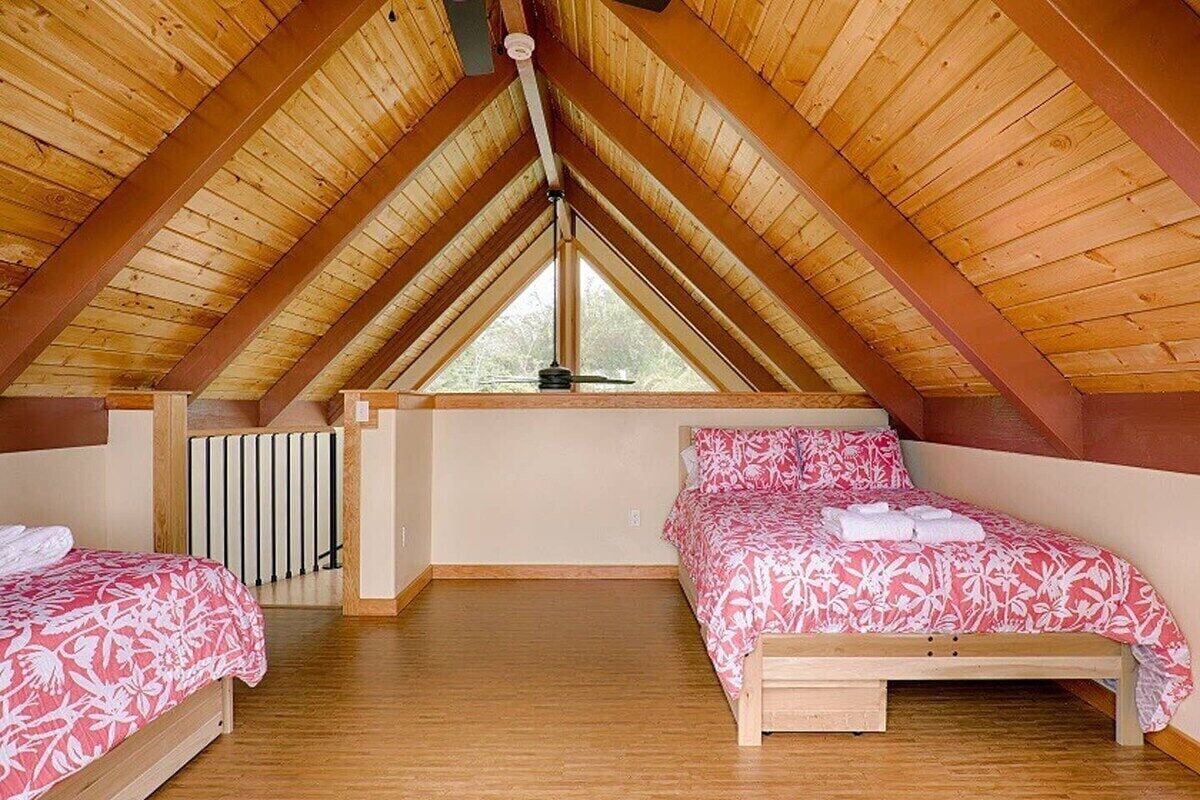 A bedroom with two beds, wooden beams, a window, and a ceiling fan.