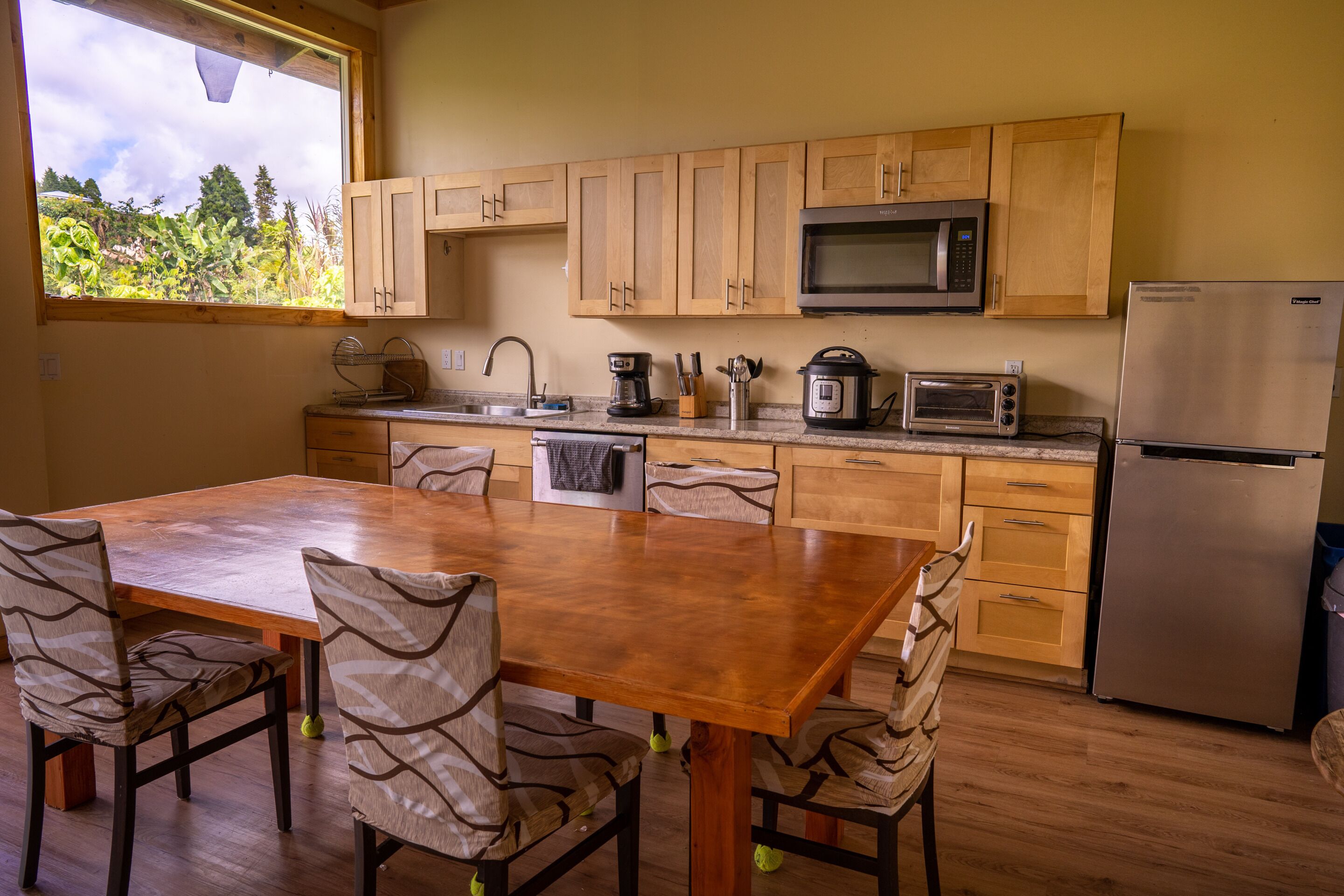 A kitchen with wooden cabinets, a stainless steel refrigerator, a microwave, a coffee maker, and a sink.