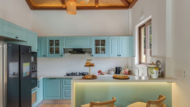 A kitchen with teal cabinets, a black refrigerator, a central island with seating, and a window with a view. - Villa Daffodil hosted by Masaya Stays (Vagator)