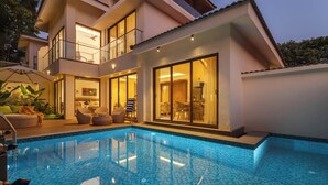 A modern two-story house with a swimming pool, large glass doors, and a well-lit interior. - Villa Daffodil hosted by Masaya Stays (Vagator)