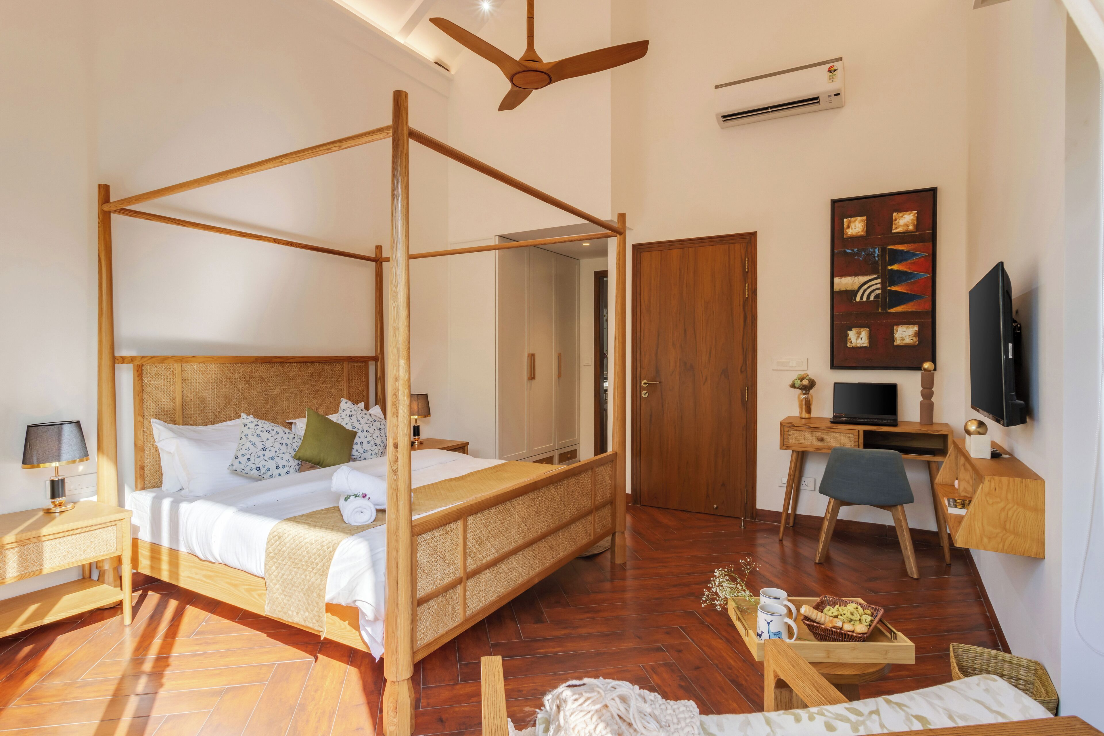 A spacious room with a four-poster bed, a desk with a computer, a television, and a small seating area.