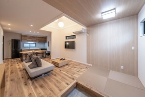 Un salon moderne avec un canapé, une table basse et un coin repas, la cuisine étant visible au fond.