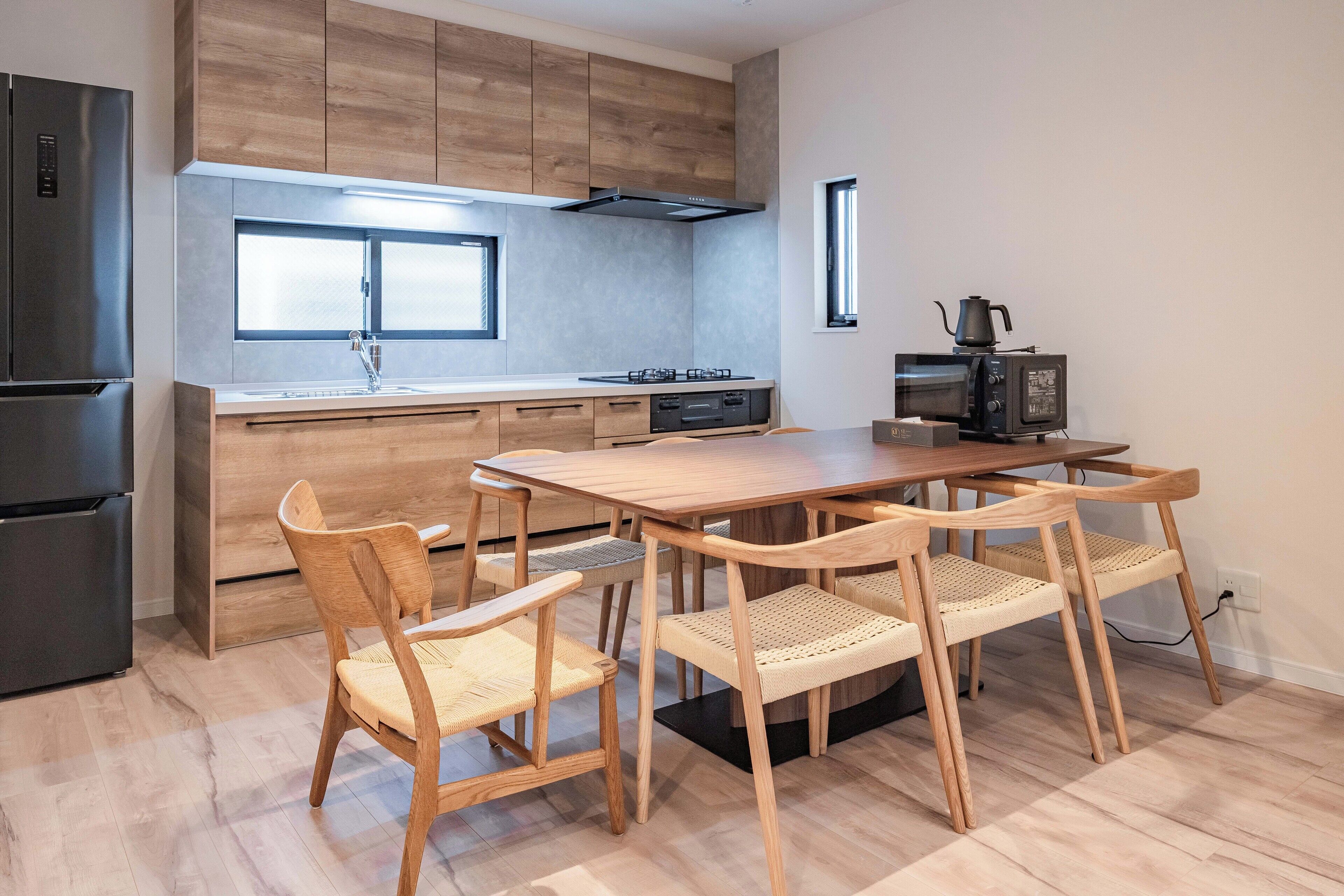 Une cuisine moderne avec des meubles en bois, une cuisinière encastrée et une table à manger avec quatre chaises.