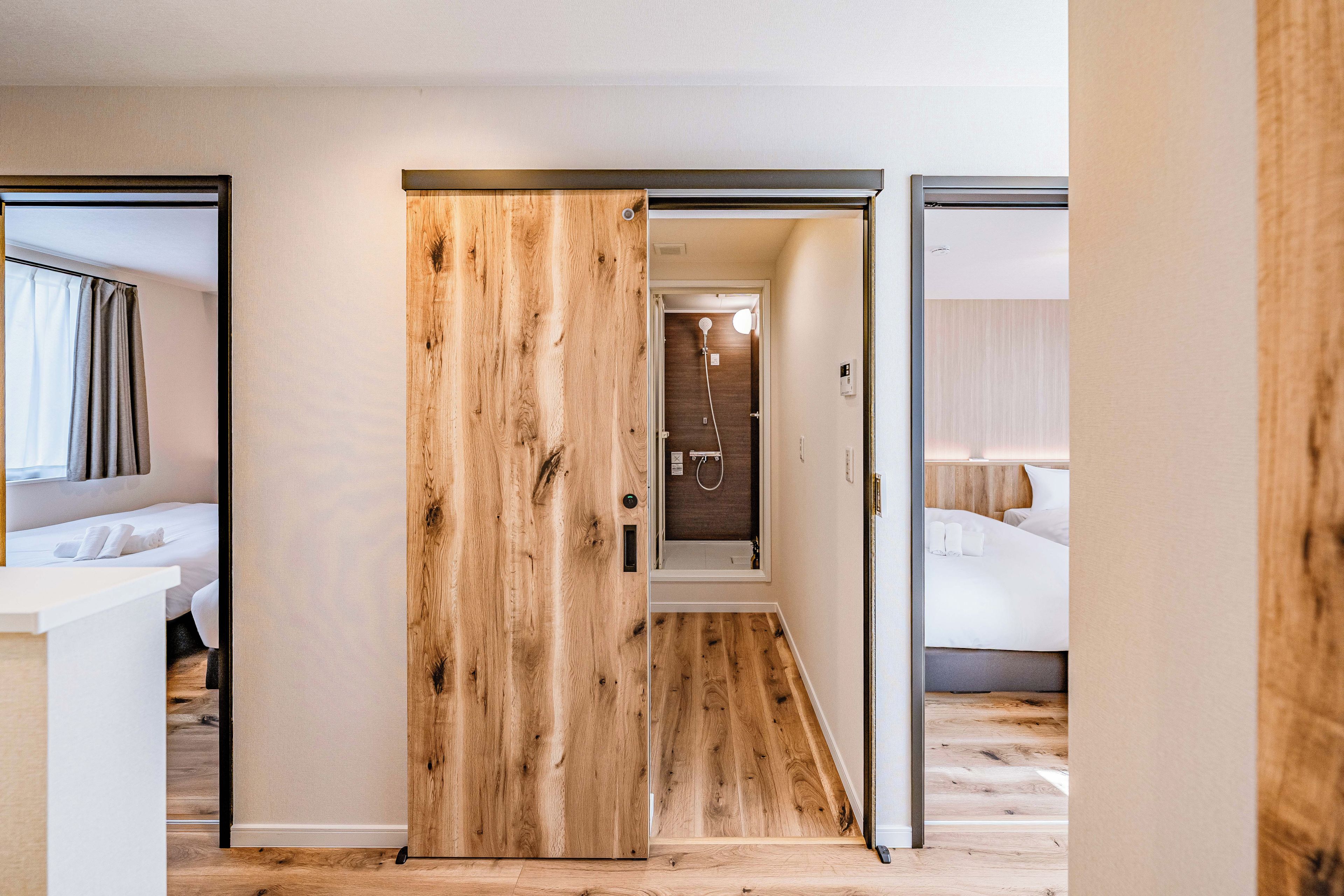 A hotel room with a wooden floor, a bed with white linens, and a bathroom with a shower.
