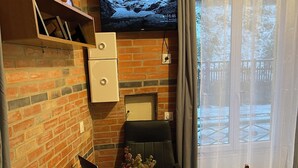 Un salon chaleureux avec un mur en briques, un téléviseur à écran plat fixé au-dessus d’une cheminée, une table à manger en bois ornée d’un vase de fleurs et un fauteuil.