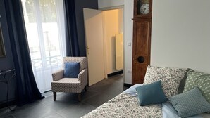 Un salon avec un canapé à motifs, un fauteuil à motifs, une horloge en bois et une porte donnant sur une autre pièce.