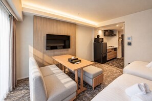 Een hotelkamer met een bank, een tafeltje, een televisie, een kitchenette en een bed.