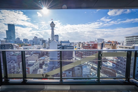 A cityscape with a prominent tower and various buildings, viewed from a balcony with a glass railing.