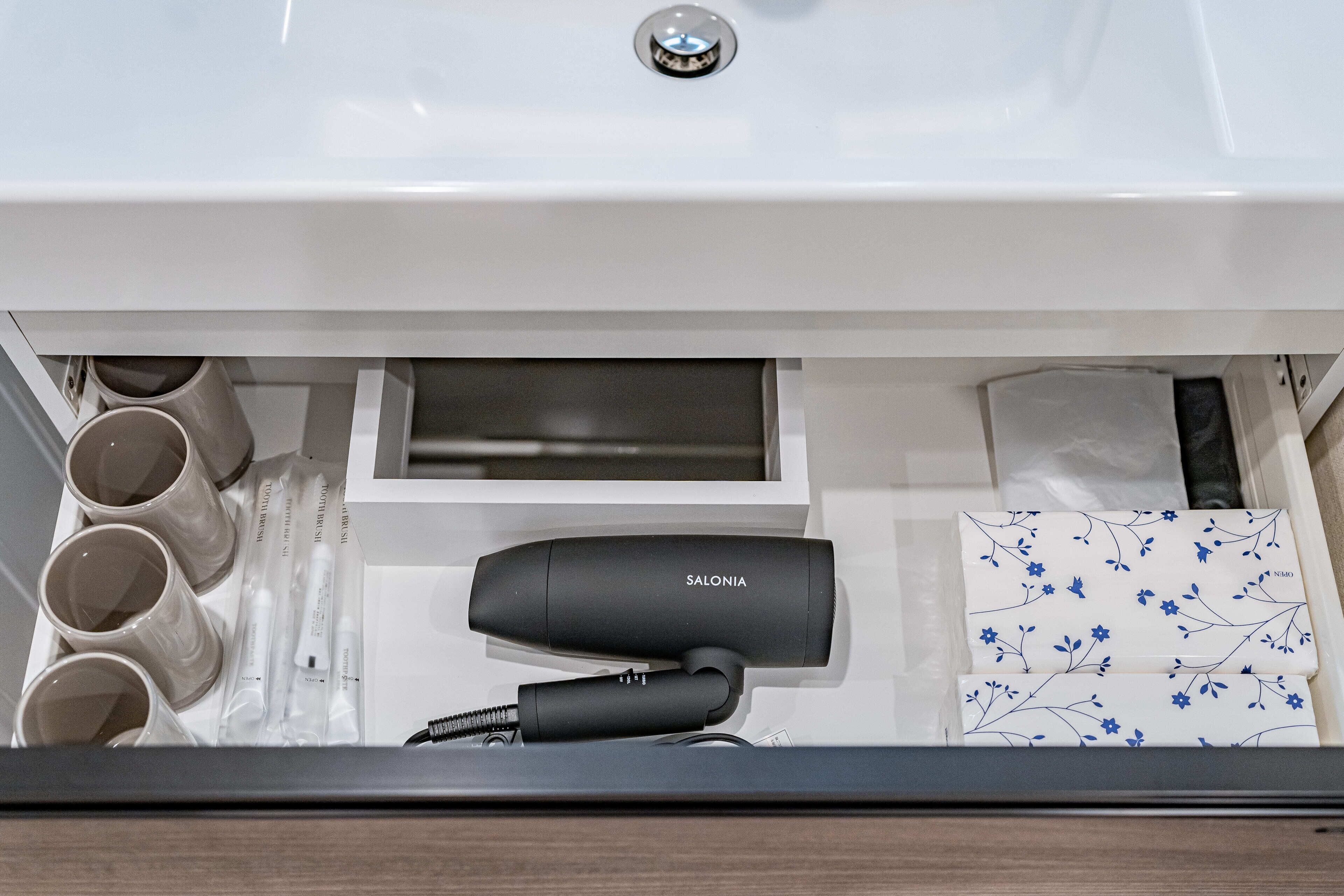 Un baño con lavamanos blanco, secador de pelo y varias tazas.