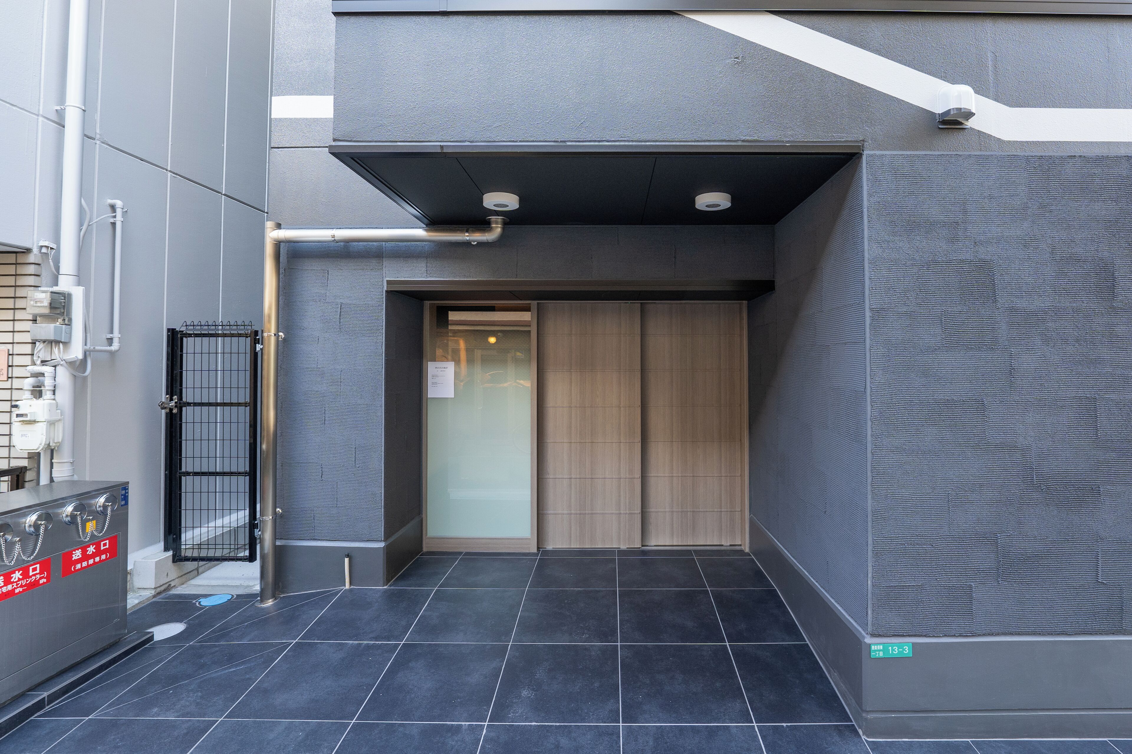 A modern building entrance with a metal gate, a tiled floor, and a sign indicating room number 13-3.