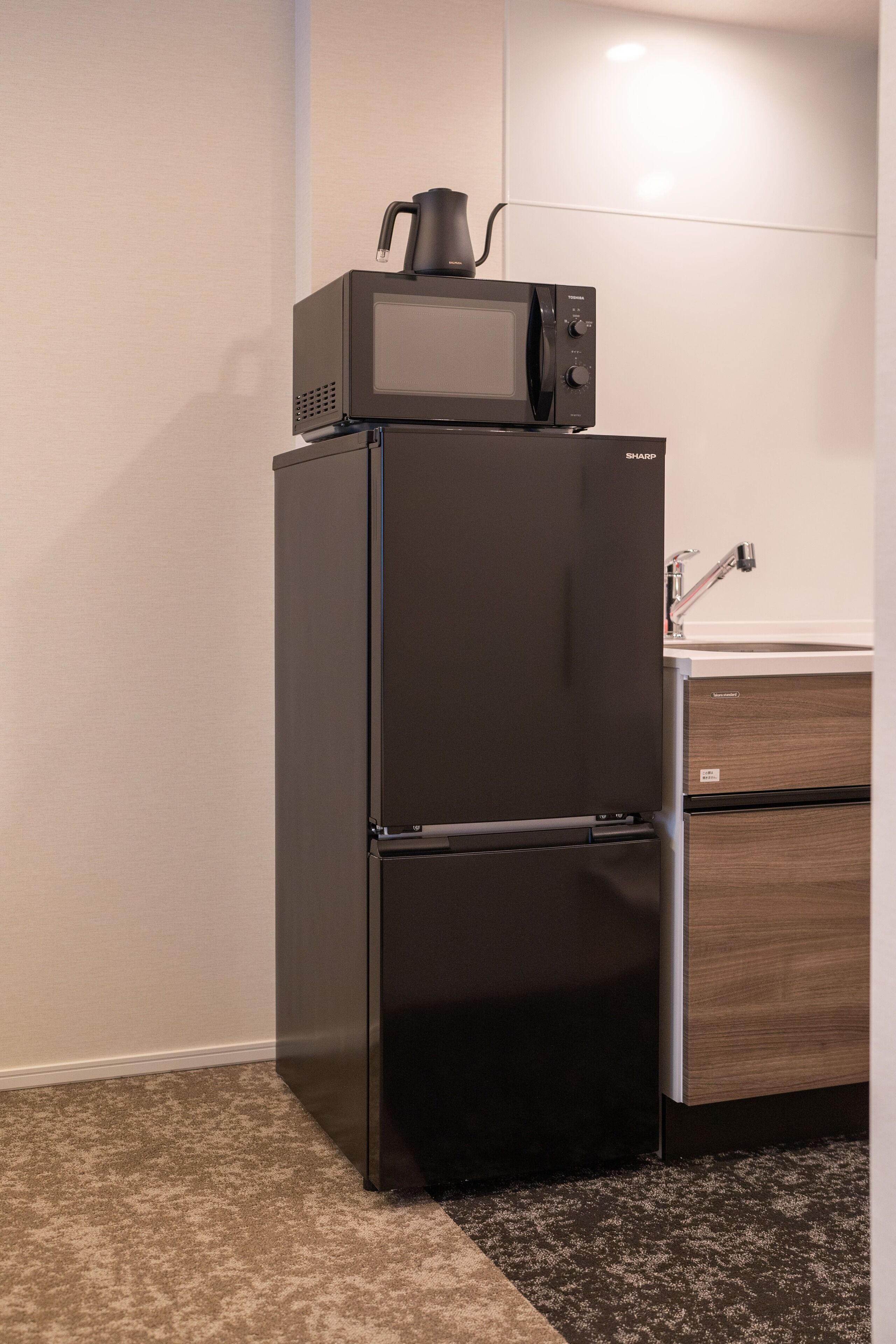 A compact kitchen with a black refrigerator, a microwave, and a wooden cabinet.
