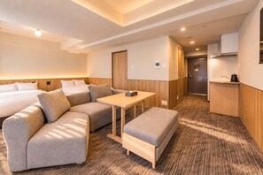 Una habitación de hotel con sofá cama, una mesita, kitchenette y suelo de madera.