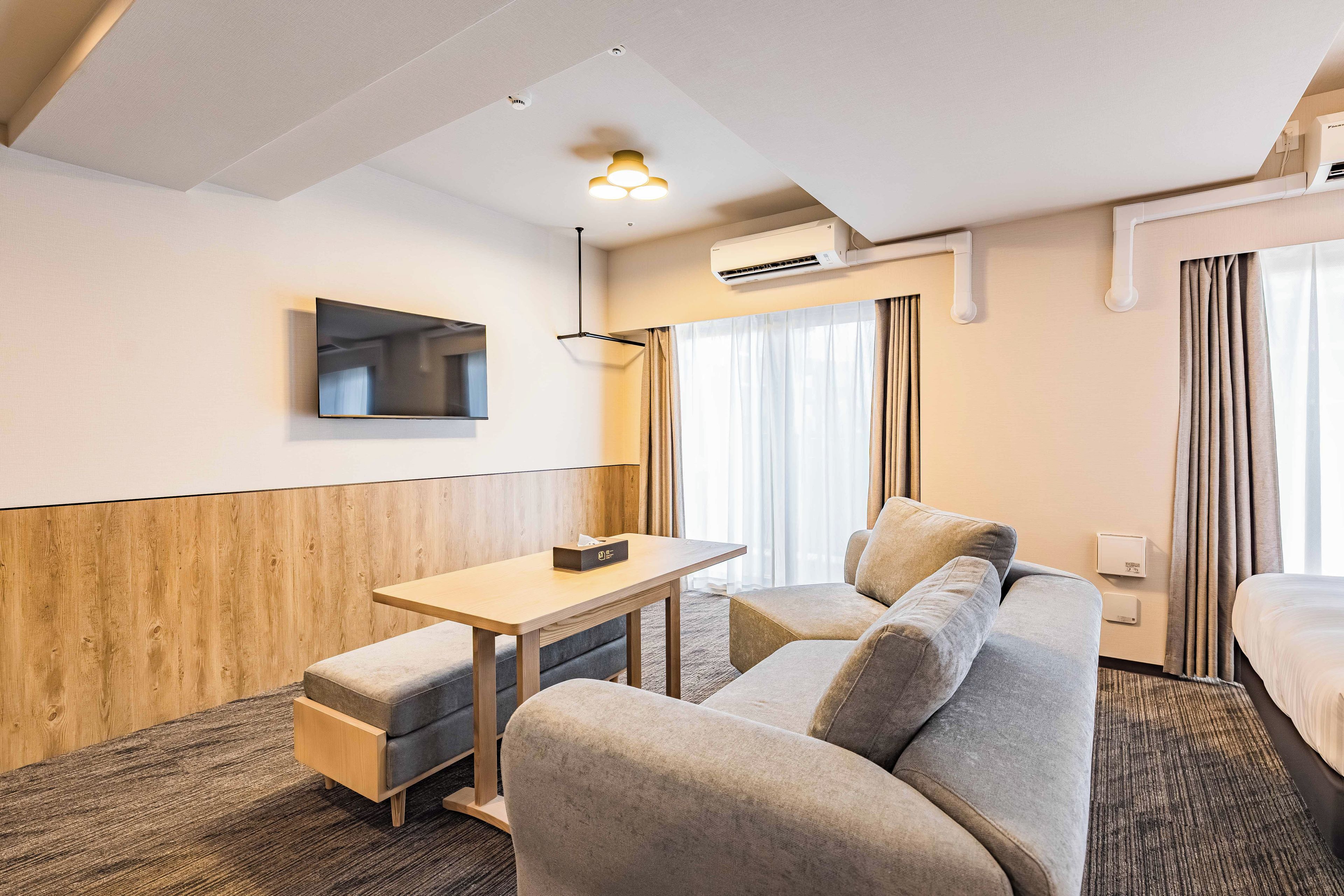 Habitación de hotel con sofá, una mesita, televisor y aire acondicionado.