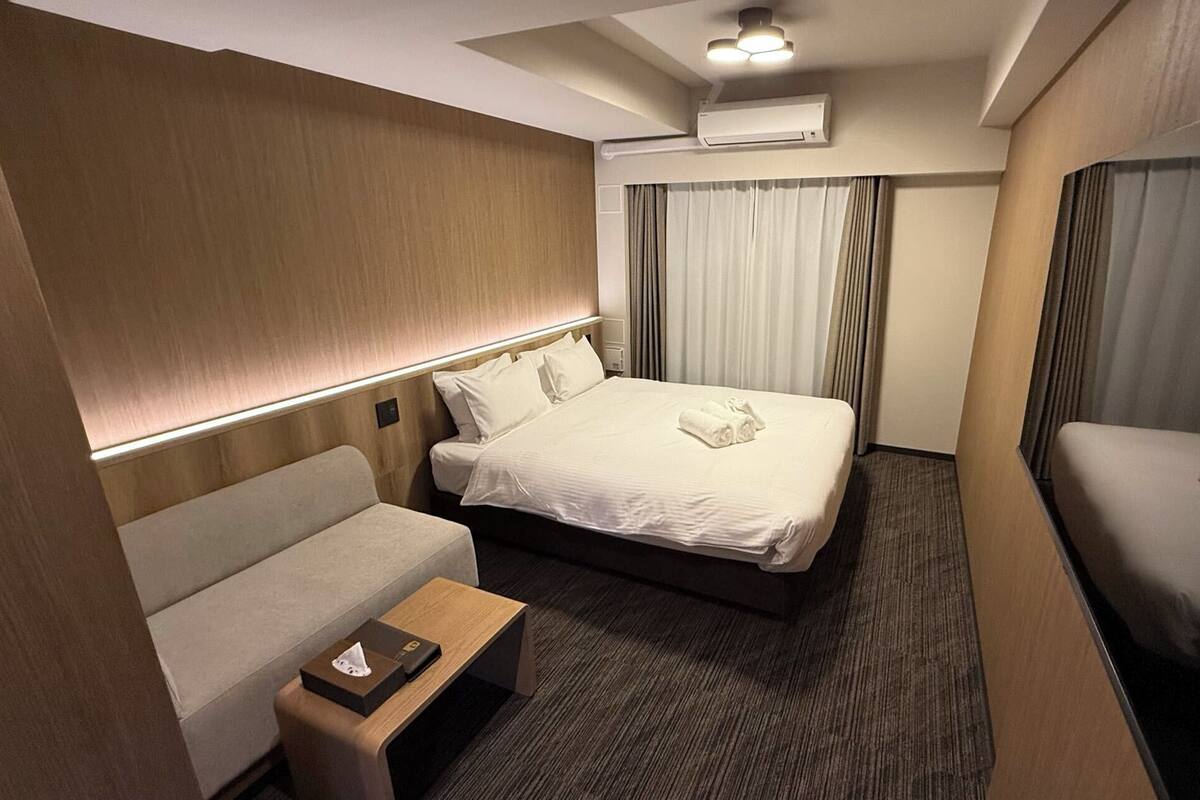 Ein Hotelzimmer mit Bett, einer Couch, einem kleinen Tisch und einer Klimaanlage.