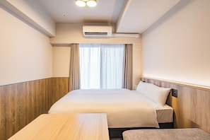 A hotel room with a bed, a bedside table, a desk, and an air conditioning unit. - Apartment Hotel 11 Namba Minami IV (Osaka)