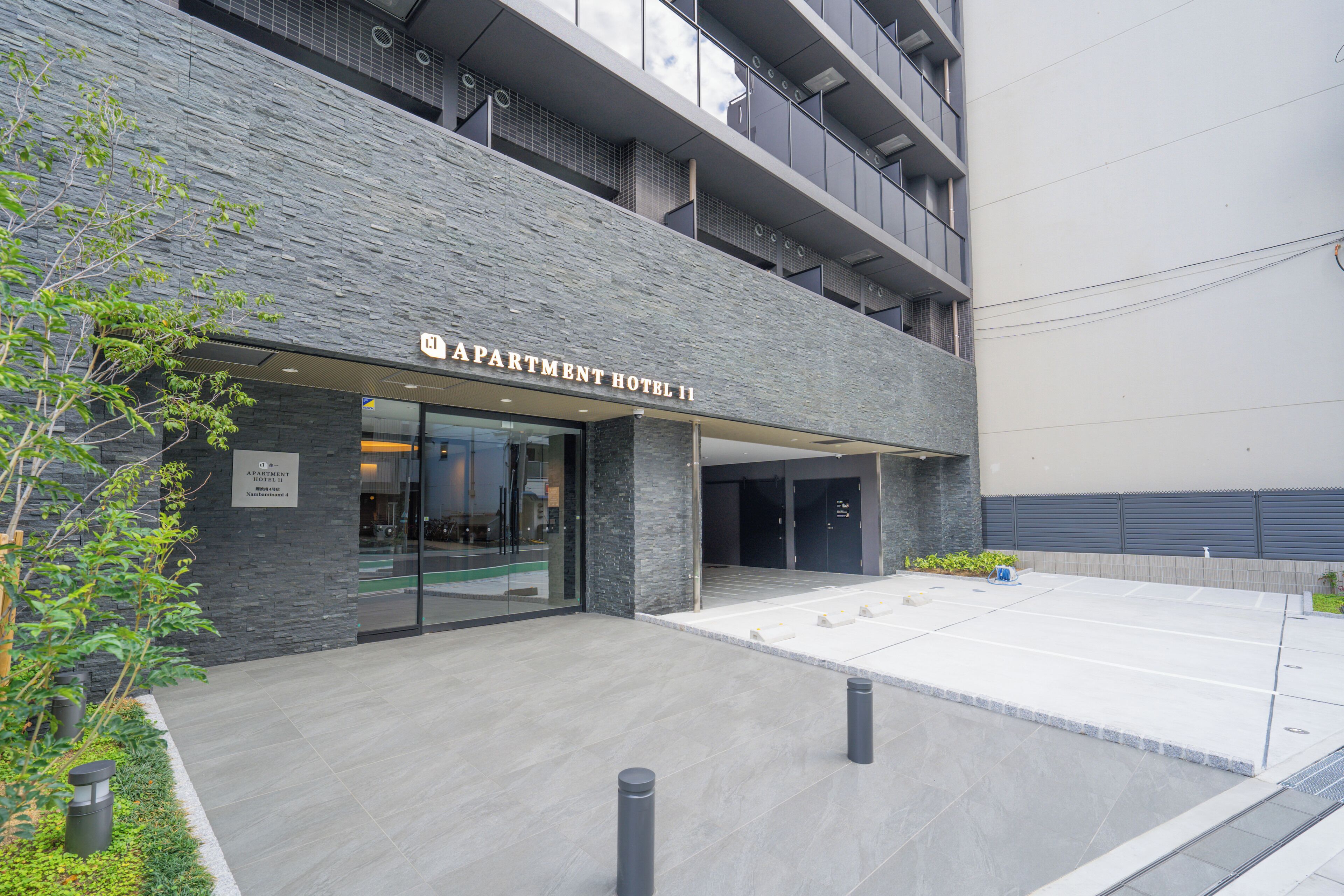 The exterior of Apartment Hotel II with a modern design, featuring a stone facade and a flat entrance area.
