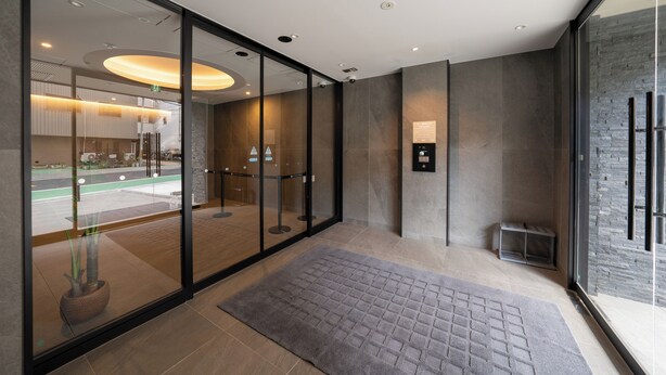 A modern hotel lobby with a glass partition, a reception desk, and a digital information board. - Apartment Hotel 11 Namba Minami IV (Osaka)