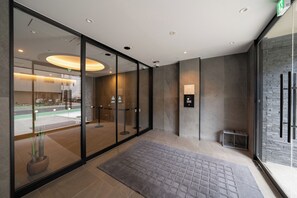 A modern hotel lobby with a glass partition, a reception desk, and a digital information board.