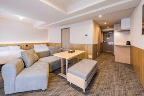 Une chambre d’hôtel avec un canapé-lit, une petite table, un banc, un coin cuisine et une salle de bain.