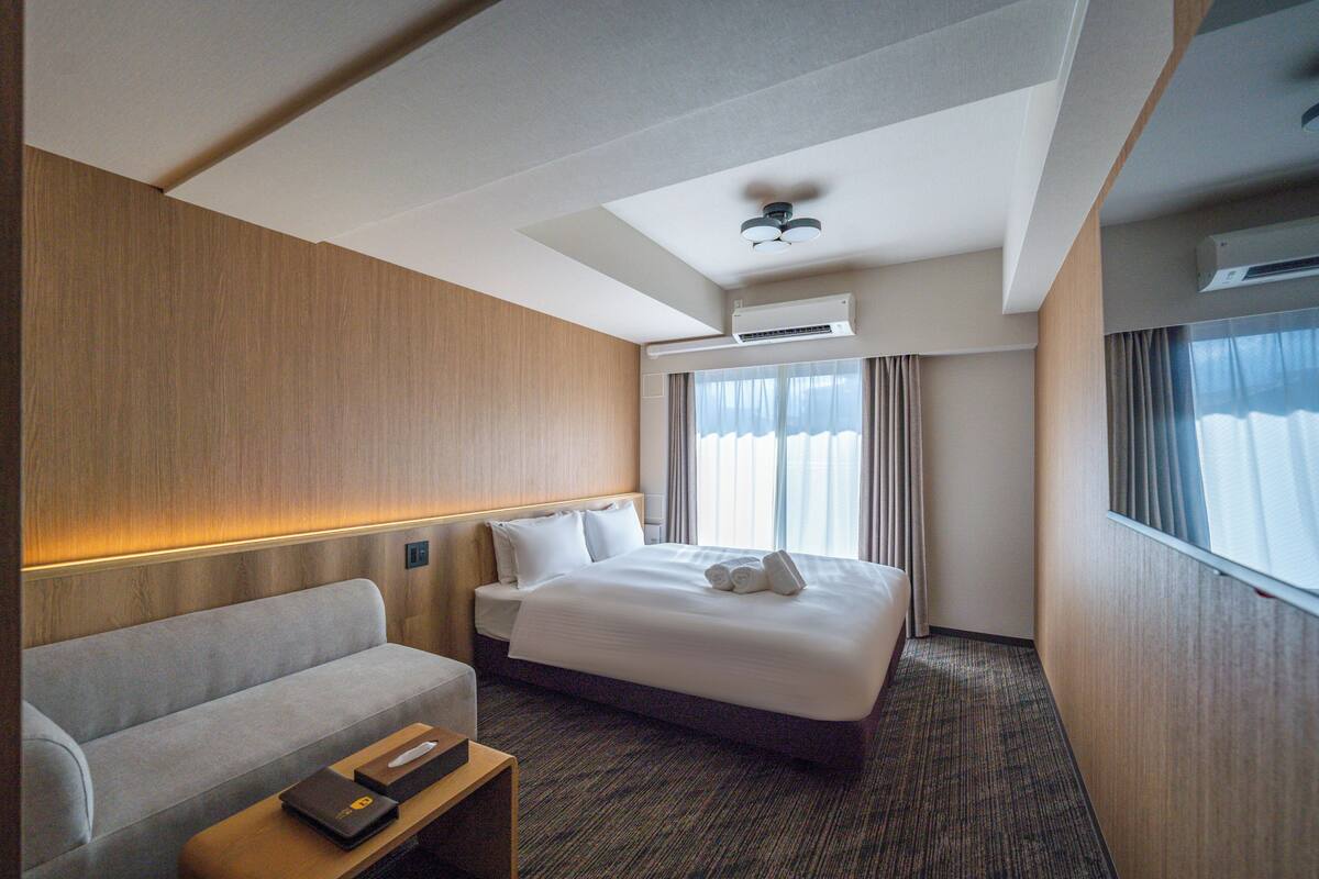Ein Hotelzimmer mit Bett, einer Couch, einem Nachttisch und einem Fenster mit Vorhängen.