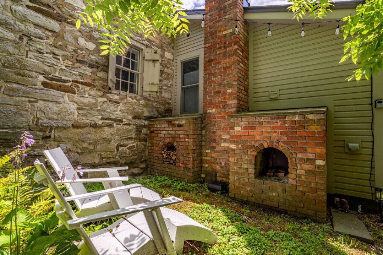 A stone building with a brick fireplace and a wooden deck with chairs.