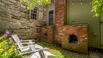 A stone building with a brick fireplace and a wooden deck with chairs.