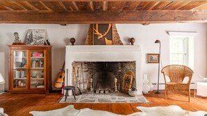 Una habitación rústica con chimenea, vigas de madera, una estantería y un sillón de mimbre.