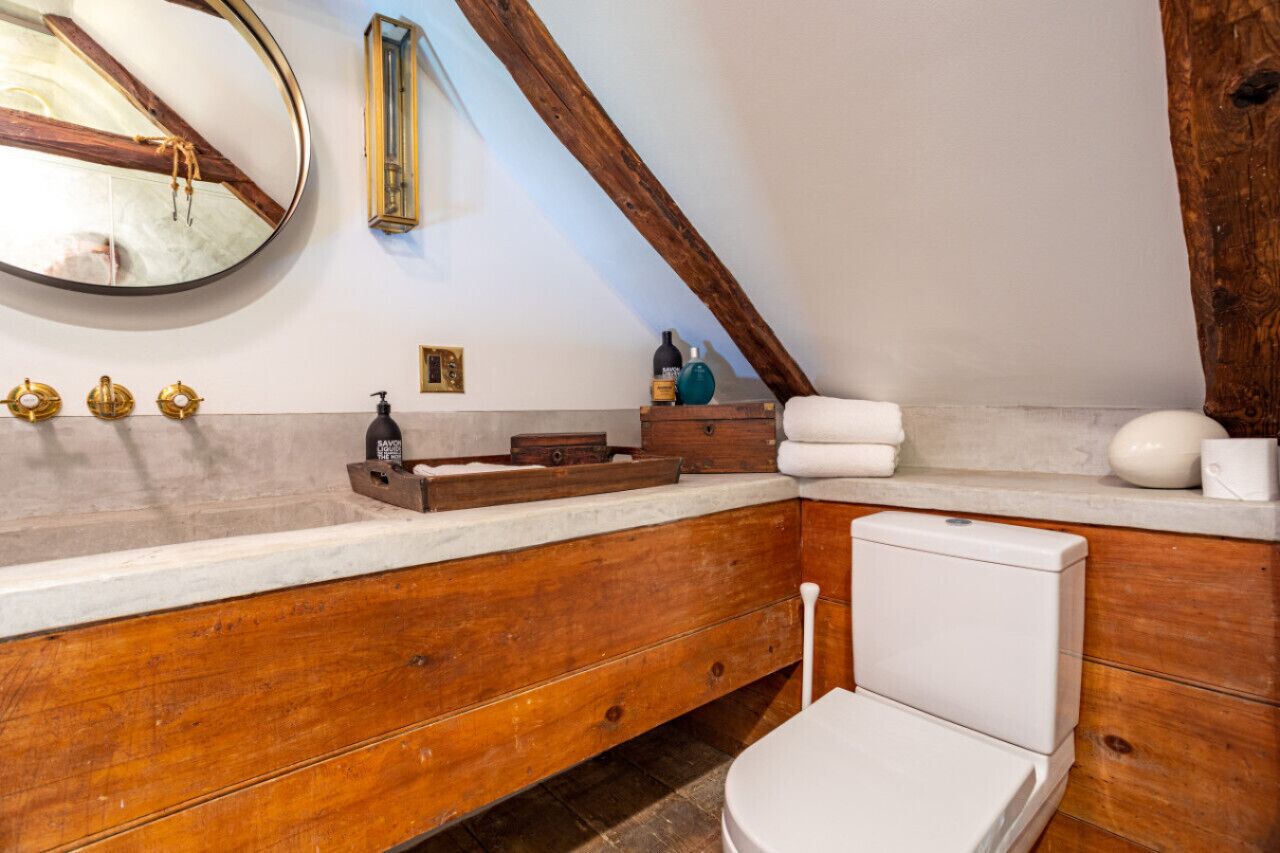 Ein Badezimmer mit einem Holzbadschränken, einem runden Spiegel, einer Toilette und einer Badewanne.