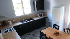 A compact kitchen with a microwave, sink, and stove. There is a dining table with chairs and a bowl on it.