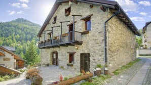 A stone building with a balcony, a cobblestone courtyard, and a mountainous backdrop. - La Baita 1800 Ski In Ski Out (Claviere)