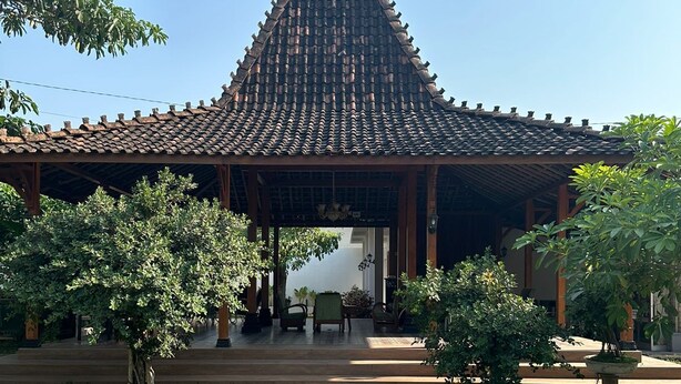 En traditionell paviljong med ett tak täckt av takpannor, omgiven av grönska och en stenlagd gångväg.