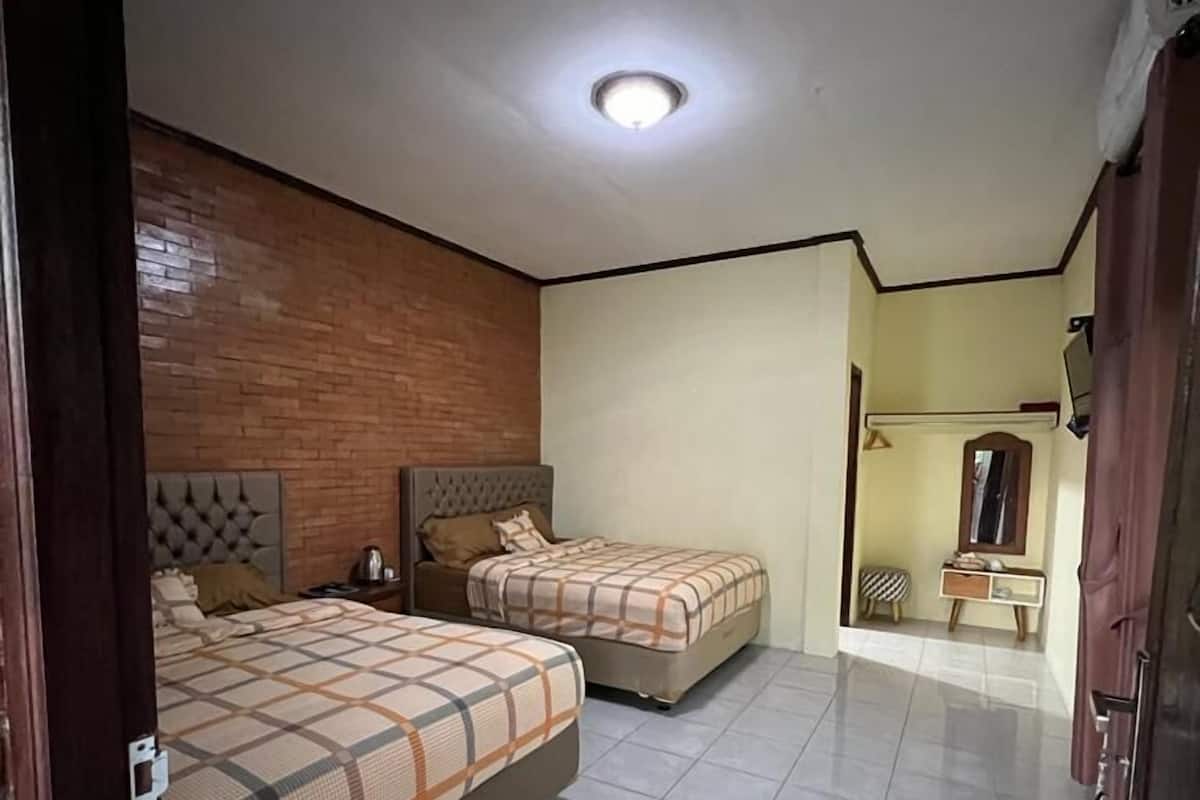 A bedroom with two beds, a wooden accent wall, a tiled floor, and a small bedside table with a lamp.