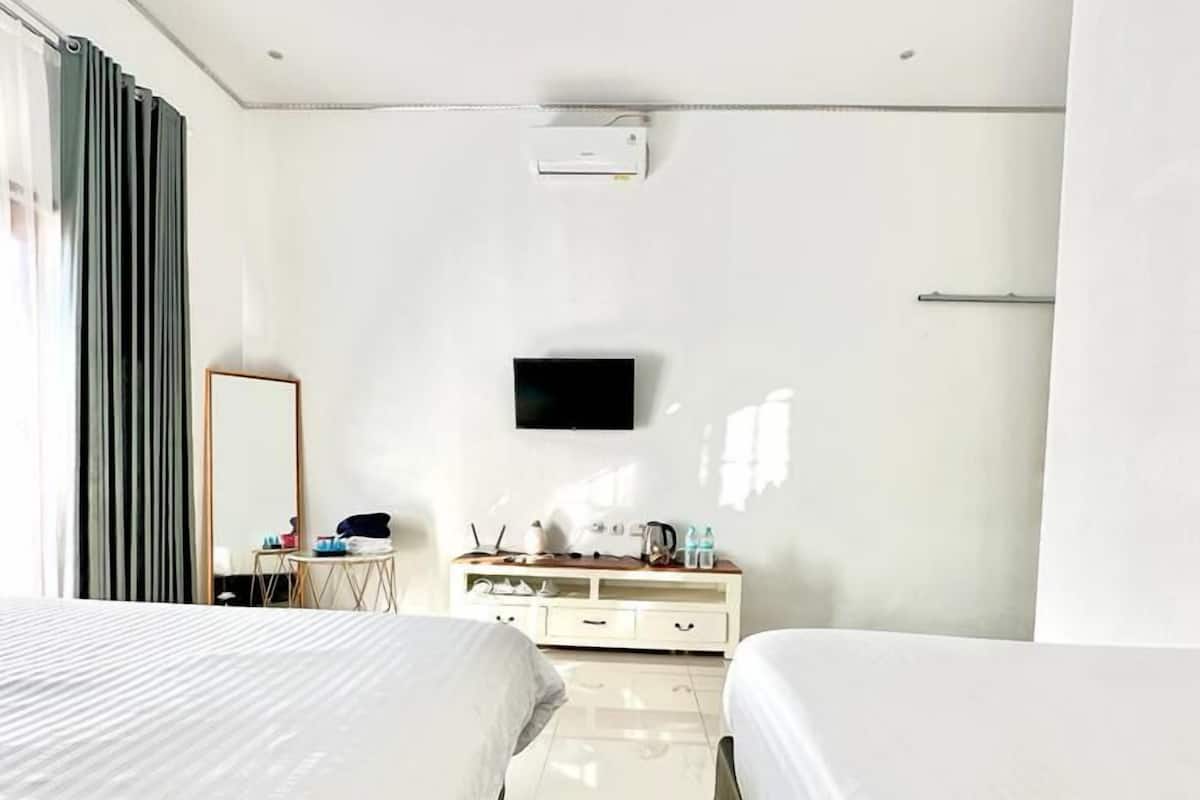 A hotel room with two beds, a flat-screen TV mounted on the wall, a small table with a mirror, and a dresser.