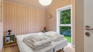 Une chambre avec un plafond en bois, une grande fenêtre, un lit avec une literie blanche, des tables de chevet et un chapeau accroché au mur.