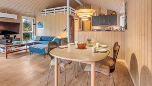 Un intérieur moderne comprenant un coin repas, un salon avec un canapé et une télévision, des murs en bois, ainsi qu’une cuisine équipée d’armoires et d’un luminaire suspendu.