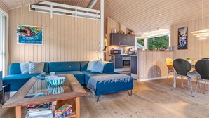 Un espace de vie moderne à aire ouverte, avec un plafond et des murs en bois, un canapé bleu, un coin repas avec des chaises et un espace cuisine.