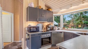 Une cuisine moderne avec des meubles de couleur sombre, un four à micro-ondes, un four traditionnel et une machine à café.