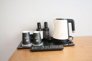 Eine Fernbedienung, zwei schwarze Tassen mit weißer Schrift, eine schwarze Flasche und ein weißer Wasserkocher auf einer schwarzen Ablagefläche.