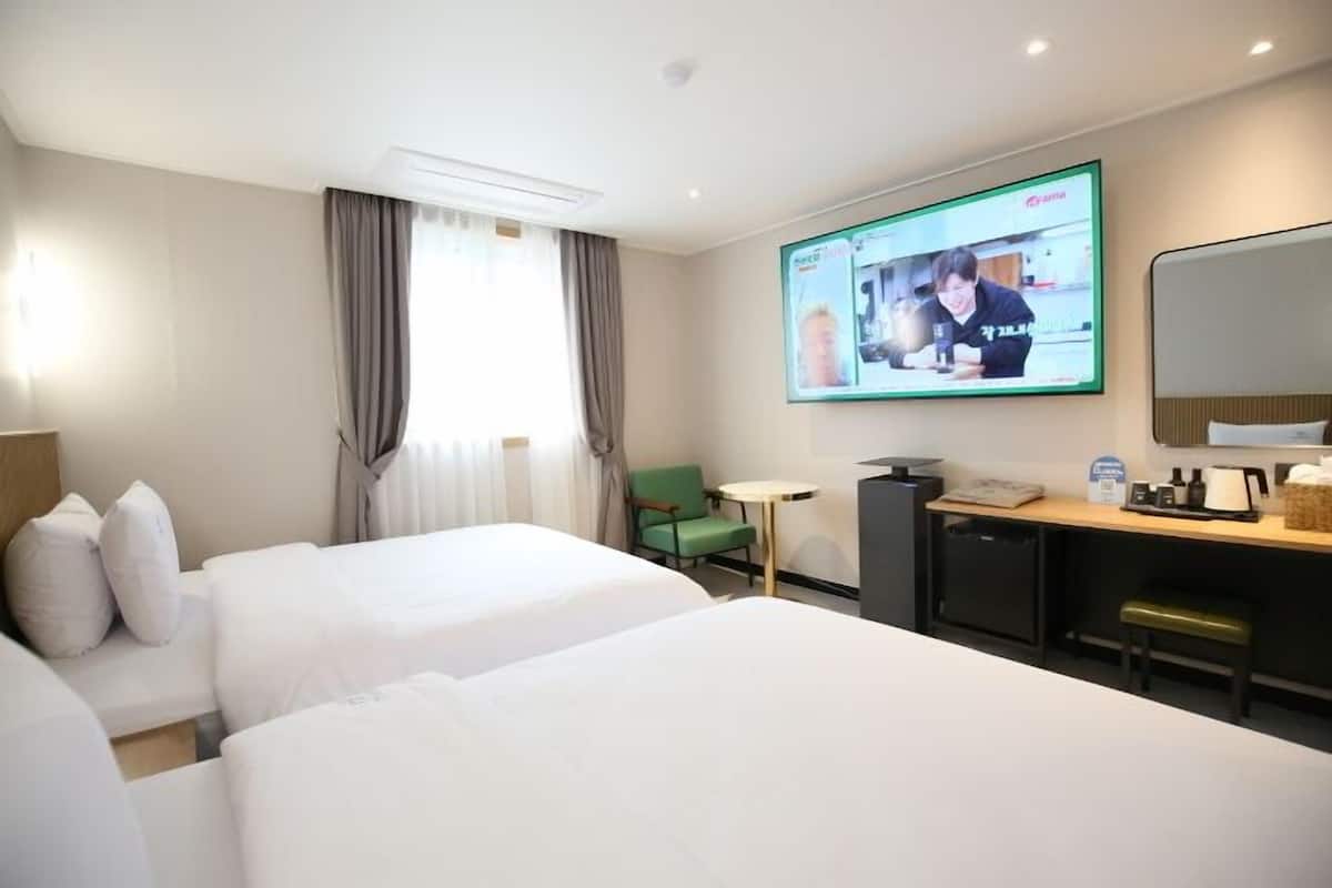A hotel room with two beds, a desk with a computer, a television mounted on the wall, and a small table with a chair.