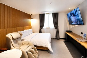 A hotel room with a bed, massage chairs, a TV, and a wooden panel wall. - Its HOTEL (Jeonju)