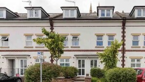 A row of terraced houses with a front garden, a parking sign, and a red car parked on the street. - Town center white house (Bournemouth)