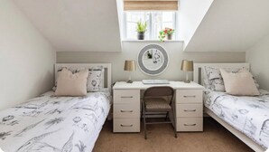A bedroom with two single beds, a desk, a chair, a window with plants, and a mirror. - Town center white house (Bournemouth)