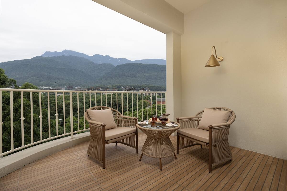 A balcony with wicker furniture, a table with drinks, and a view of mountains.