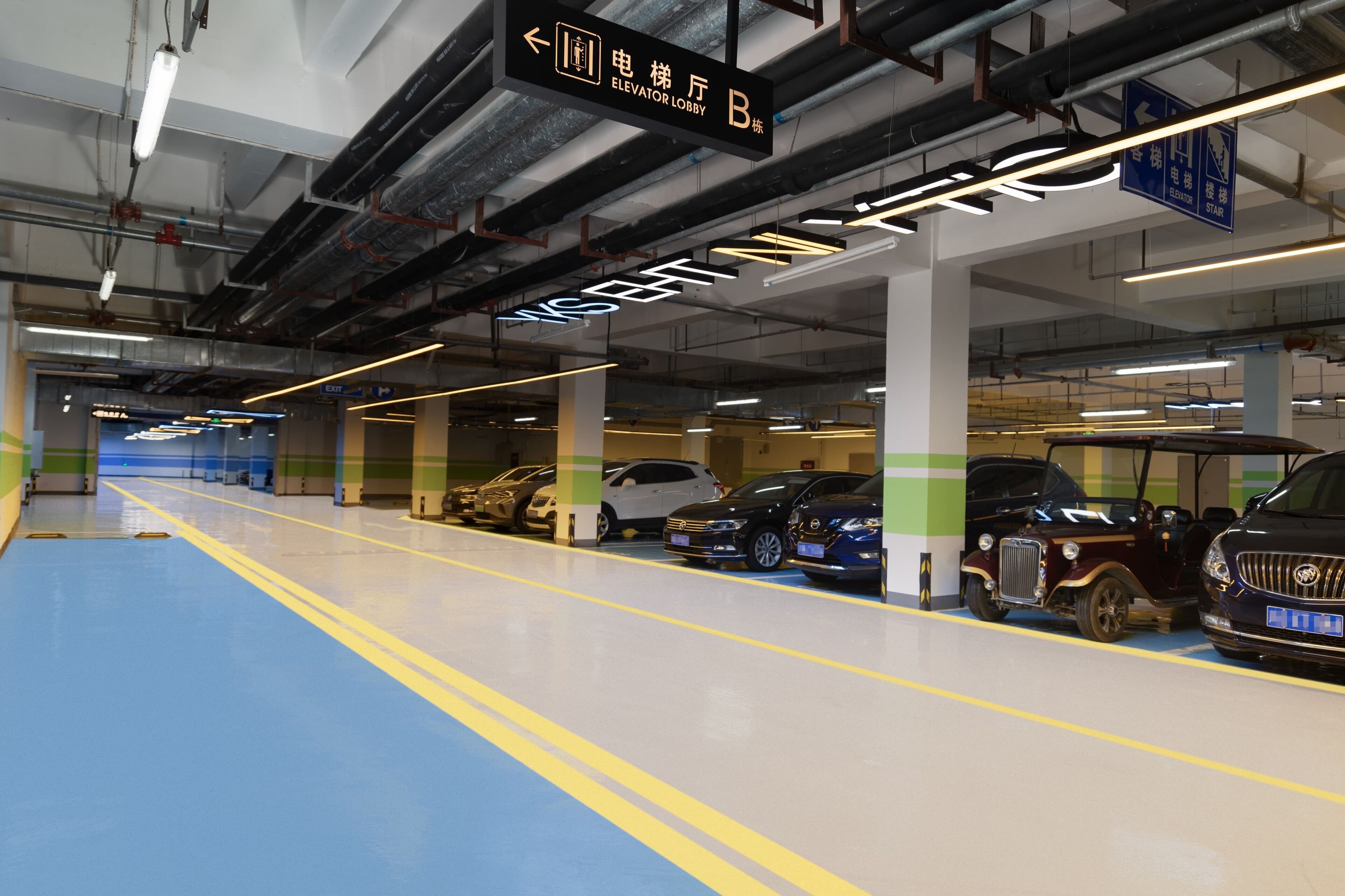 An indoor parking garage with multiple levels, clear directional signage, and a variety of parked vehicles including cars and a classic car.