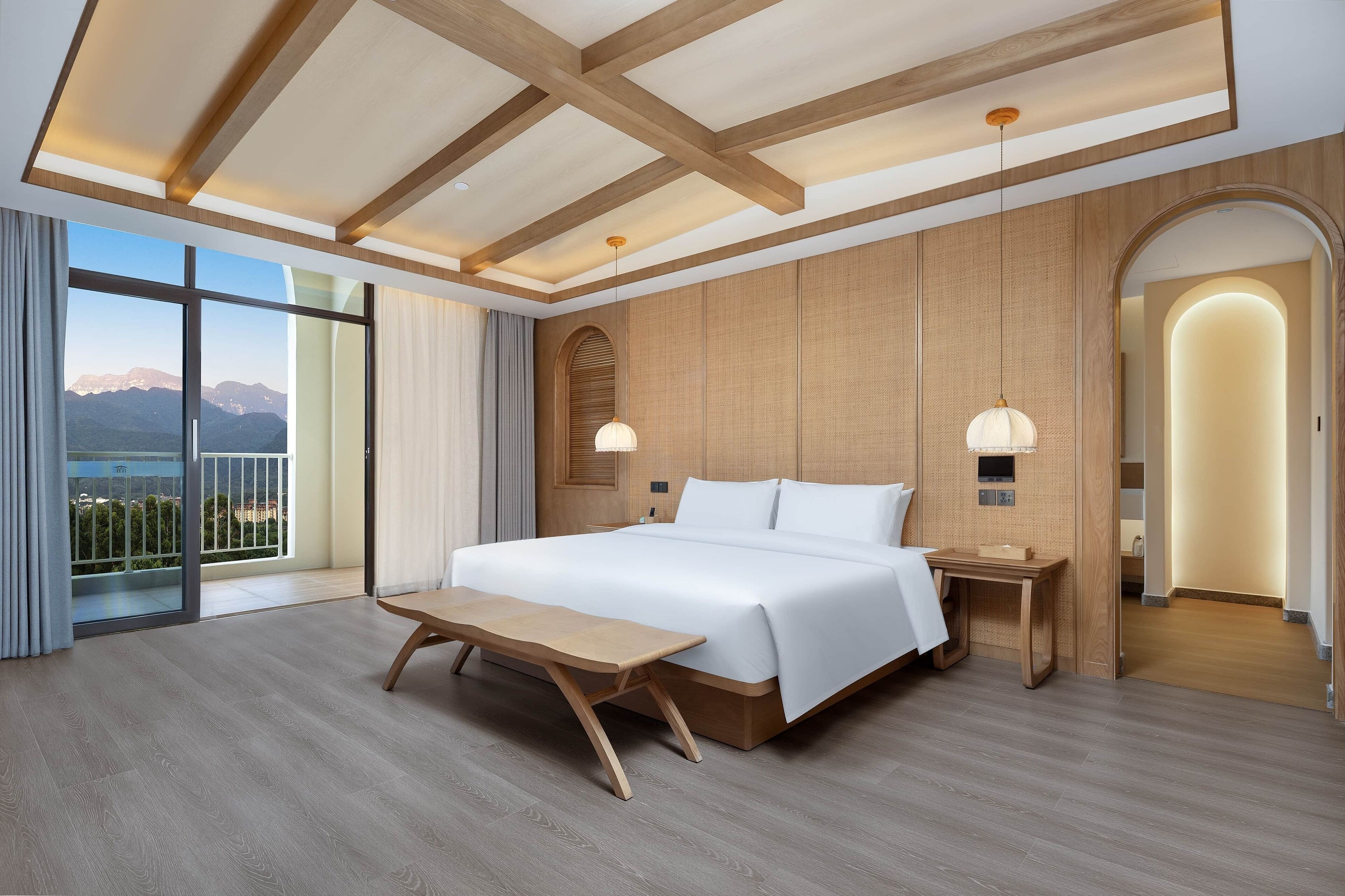 Une chambre d’hôtel moderne dotée d’un grand lit, d’un plancher en bois, de grandes fenêtres offrant une vue sur les montagnes et d’un balcon.
