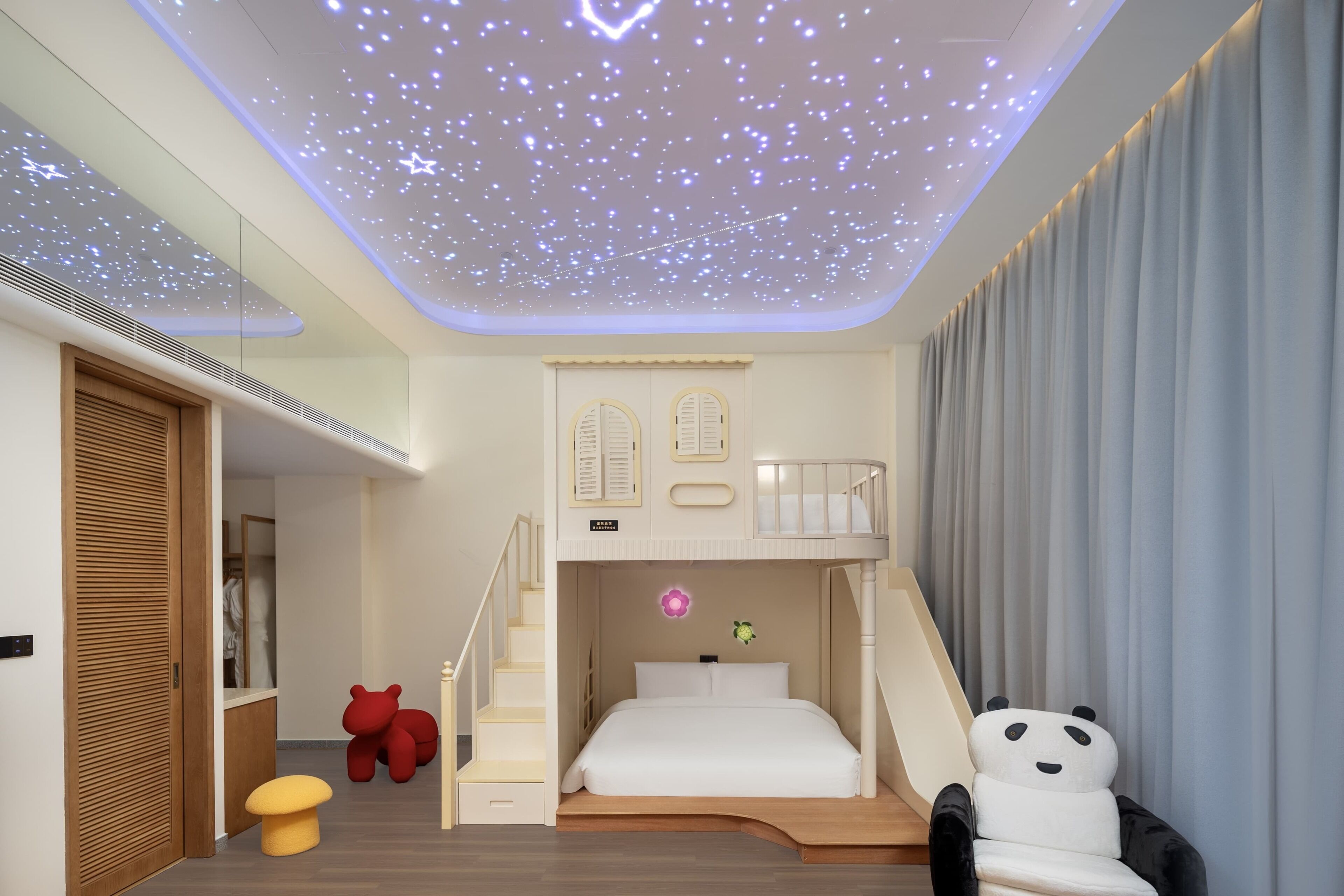 A modern bedroom with a bunk bed, a starry ceiling, and a panda-themed chair.