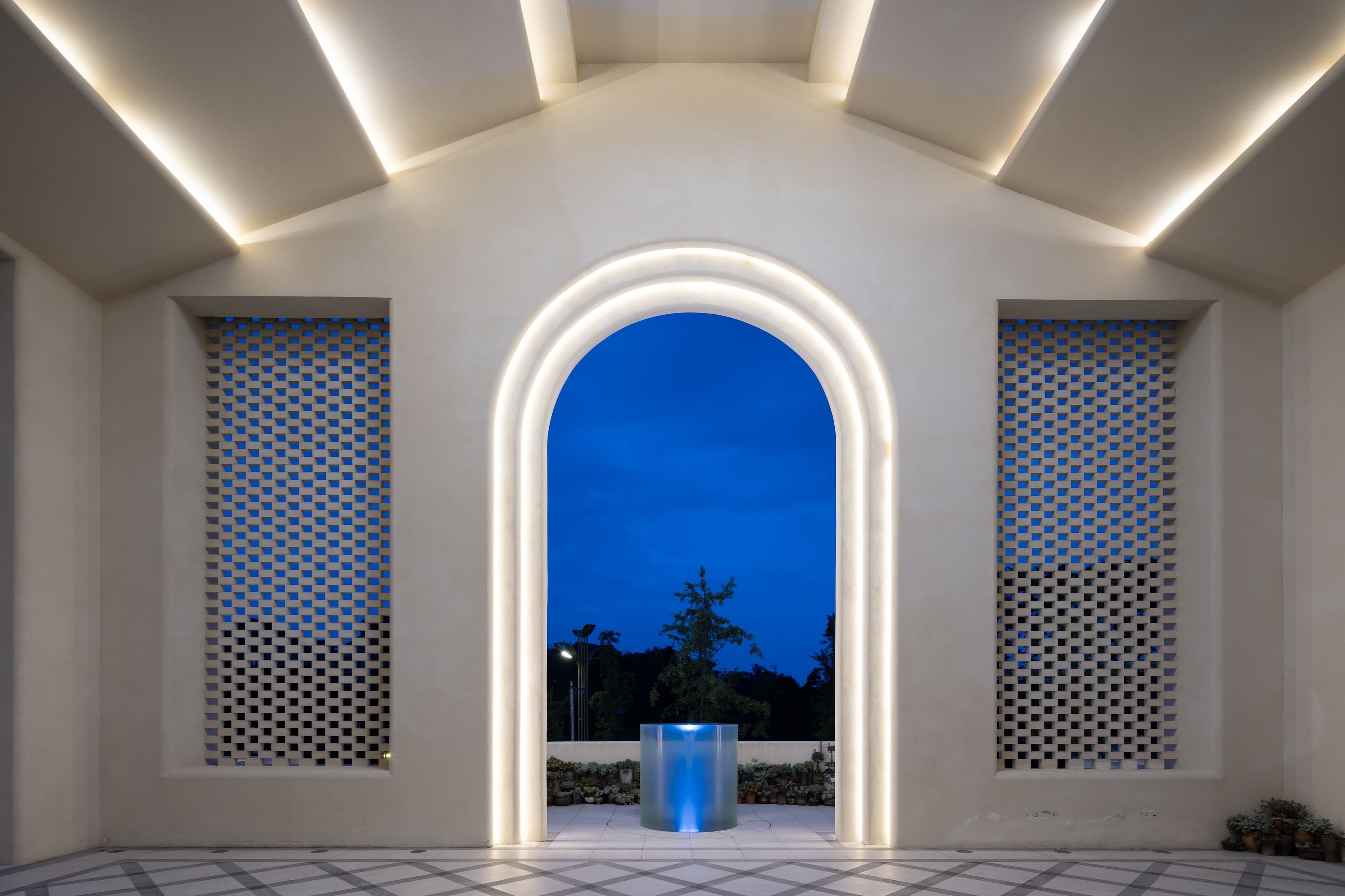 Un espace architectural moderne doté d’une arche centrale, éclairée par des luminaires encastrés, et flanqué de fenêtres à motifs.