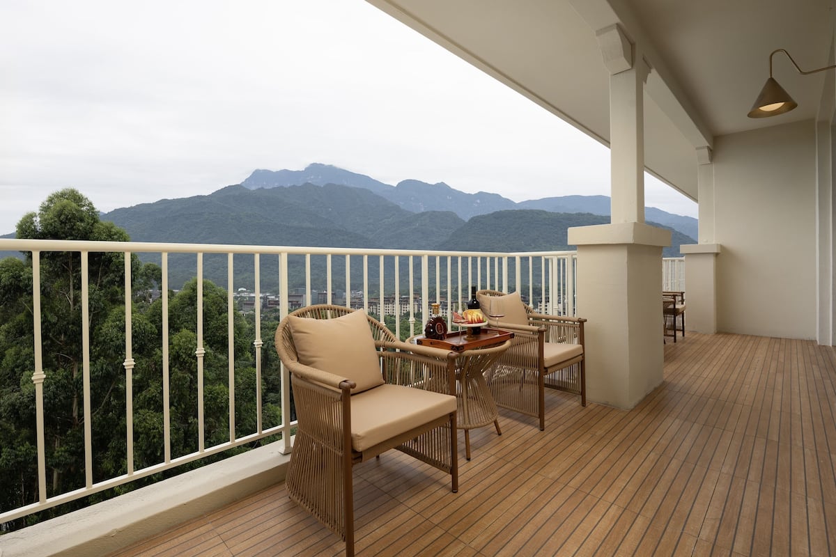 A balcony with wicker furniture, a table with a fruit bowl, and a view of mountains.